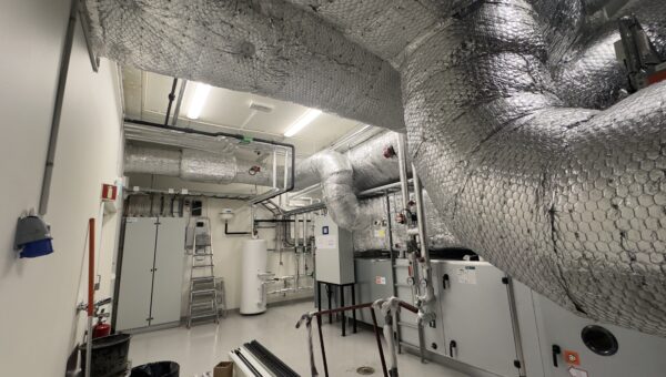 Photo réaliste d’un local technique avec unité de ventilation double flux et gaines isolées