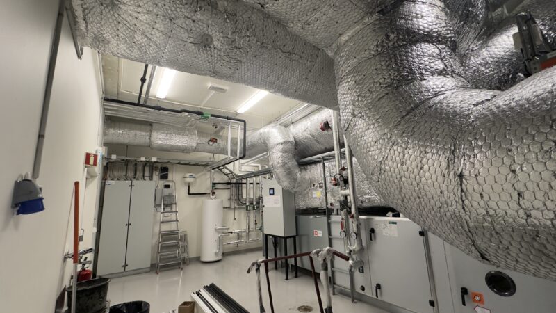 Photo réaliste d’un local technique avec unité de ventilation double flux et gaines isolées