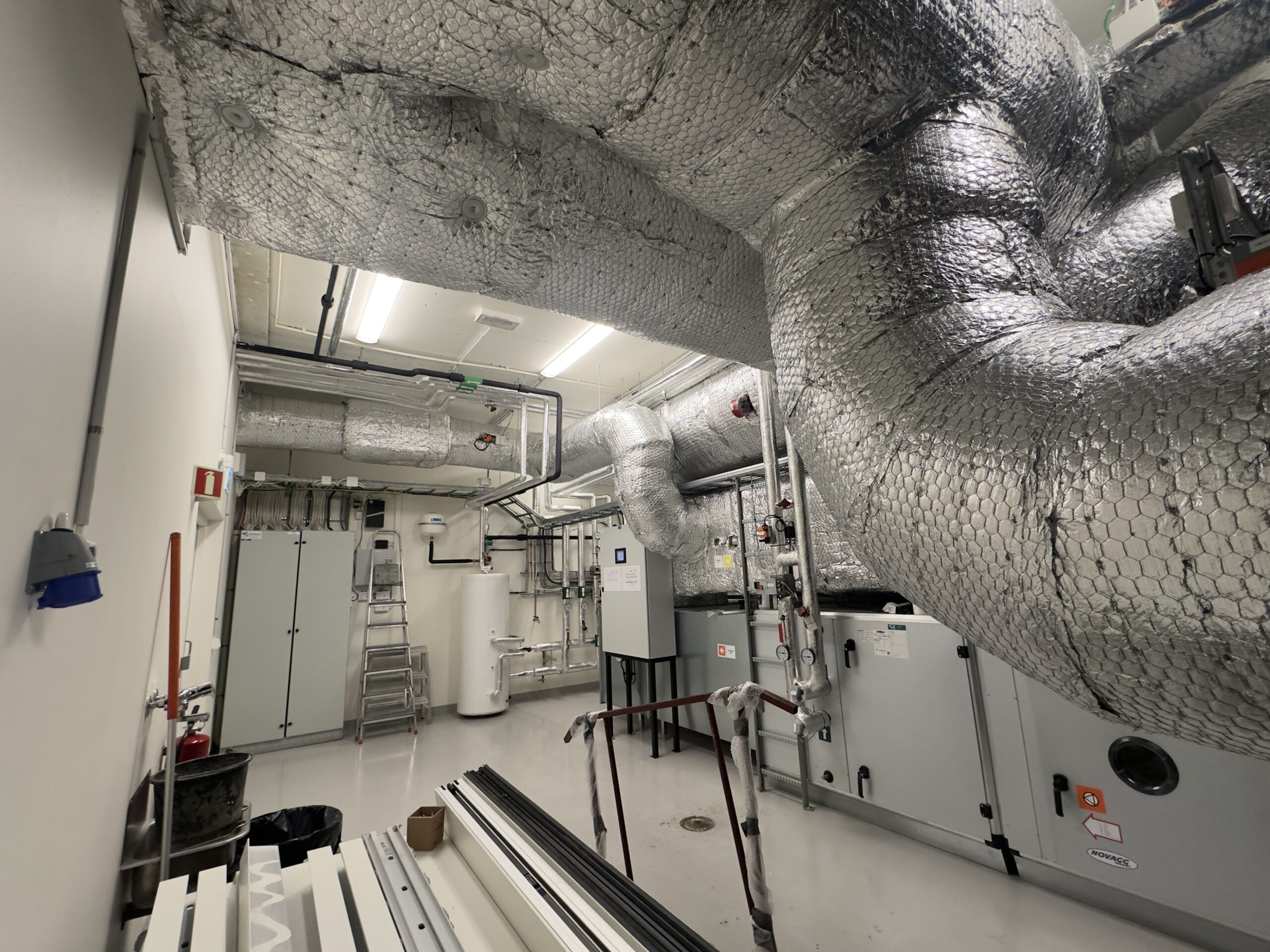 Photo réaliste d’un local technique avec unité de ventilation double flux et gaines isolées